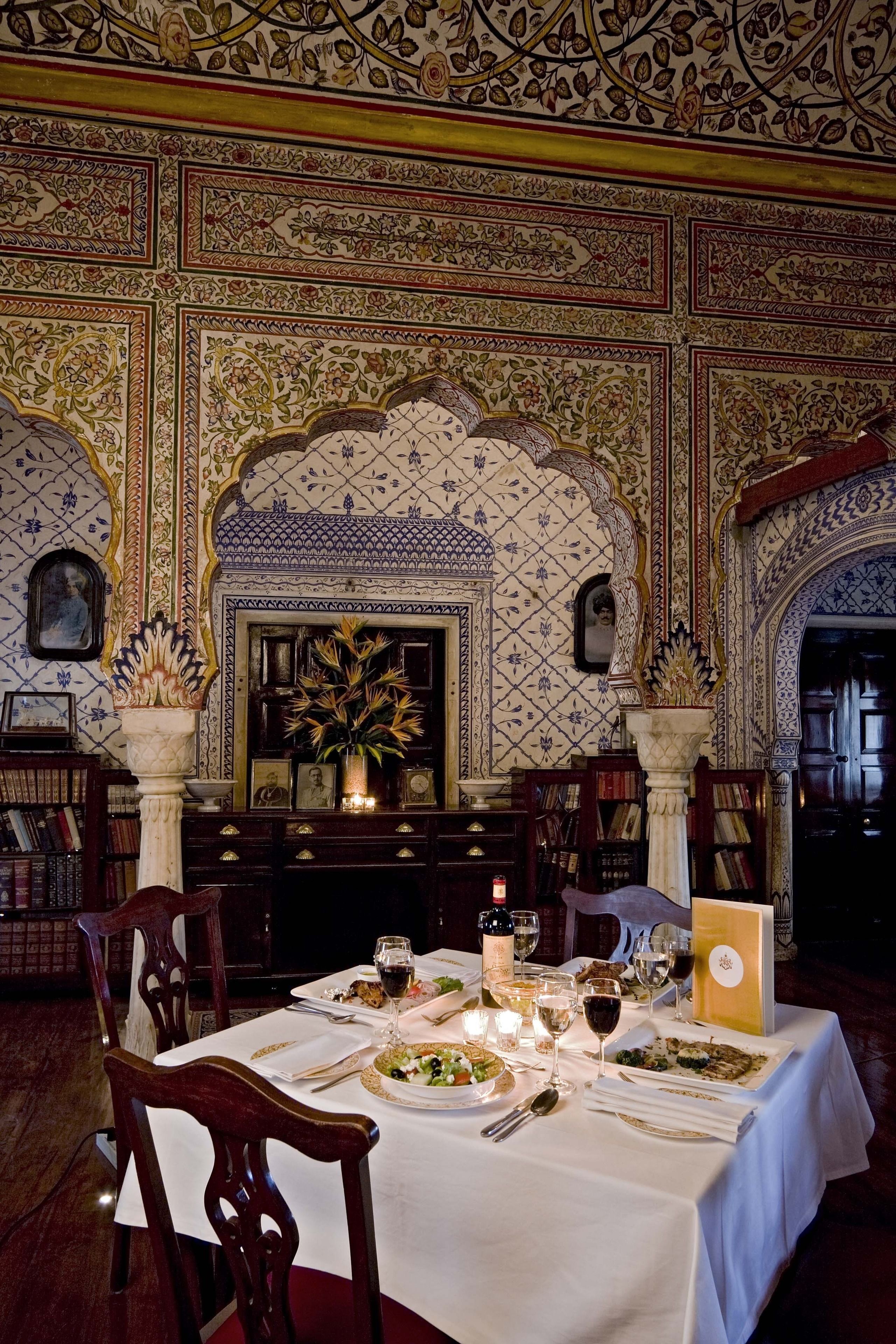 A dining area with a table set for two, surrounded by ornate wall decorations and a fireplace.