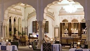 An indoor dining area with ornate arches and columns, tables set with tableware, and a person seated at a table. - Samode Haveli (Jaipur)