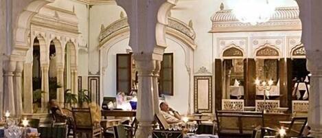An indoor dining area with ornate arches and columns, tables set with tableware, and a person seated at a table.