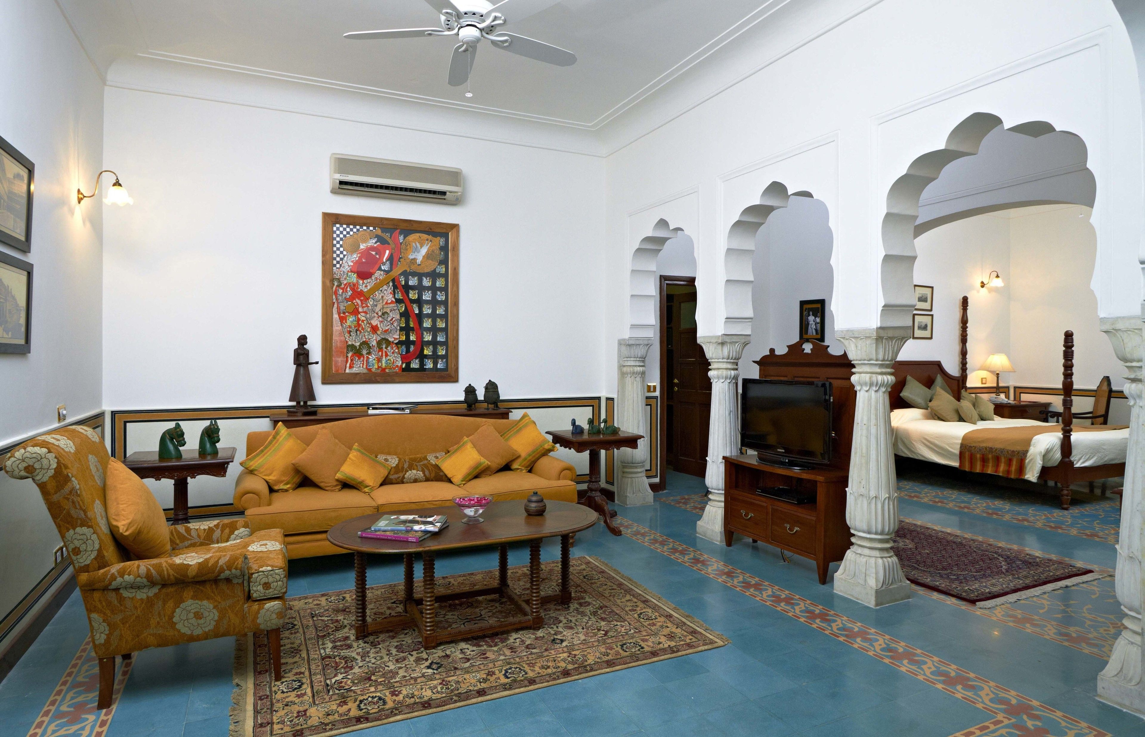 A traditional living room with a sofa, armchair, and television. There are decorative items and a patterned rug on the floor.