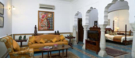 A traditional living room with a sofa, armchair, and television. There are decorative items and a patterned rug on the floor.