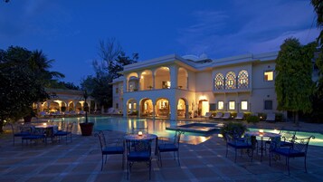 Um resort luxuoso com uma piscina grande, área de estar externa e um edifício imponente com arcos e janelas amplas.