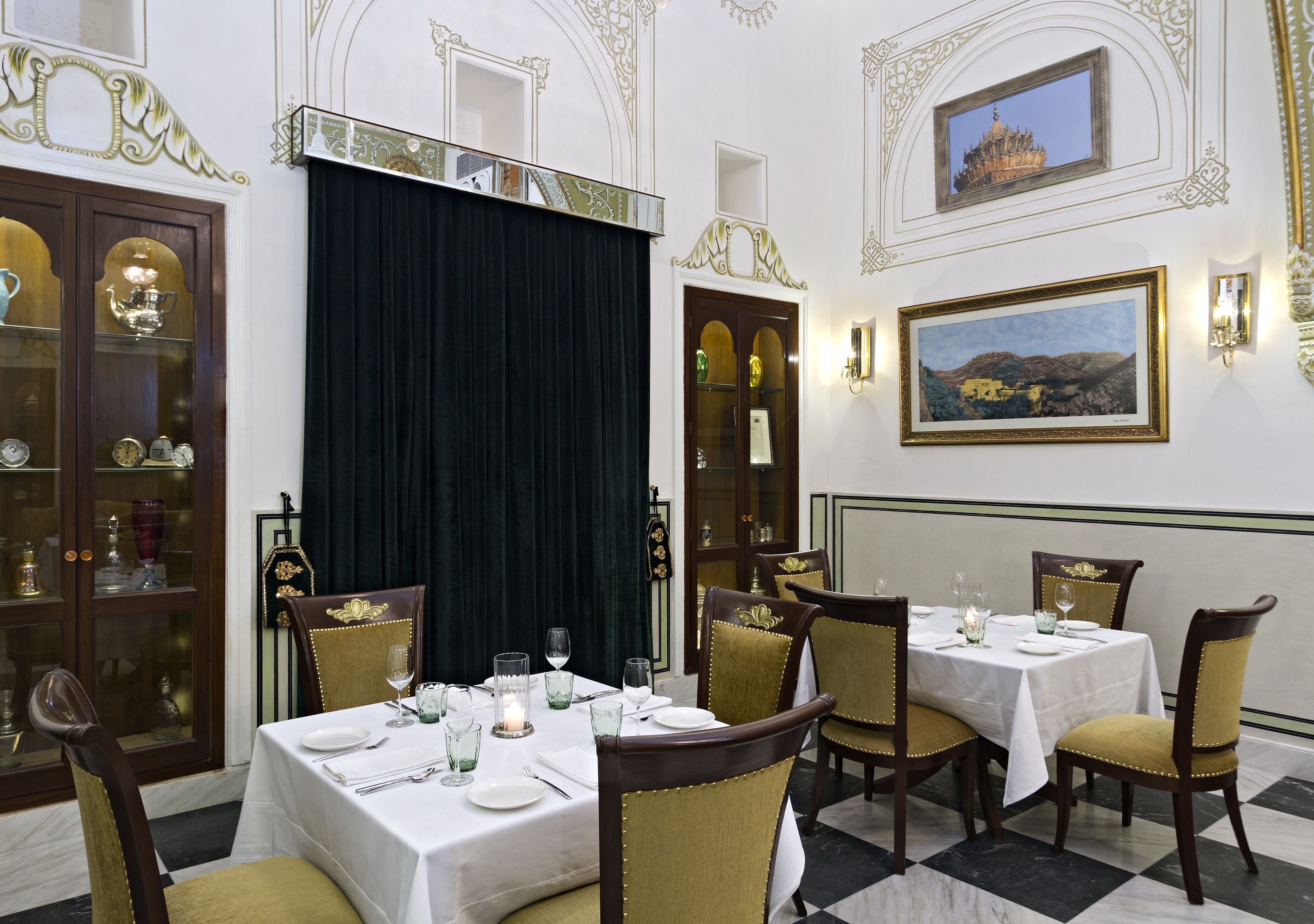 Un comedor con mesas dispuestas para cuatro, cada una con manteles blancos, sillas con detalles dorados y centros de mesa con velas.