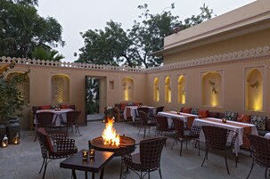 An outdoor dining area with tables and chairs, a fire pit, and decorative lighting.