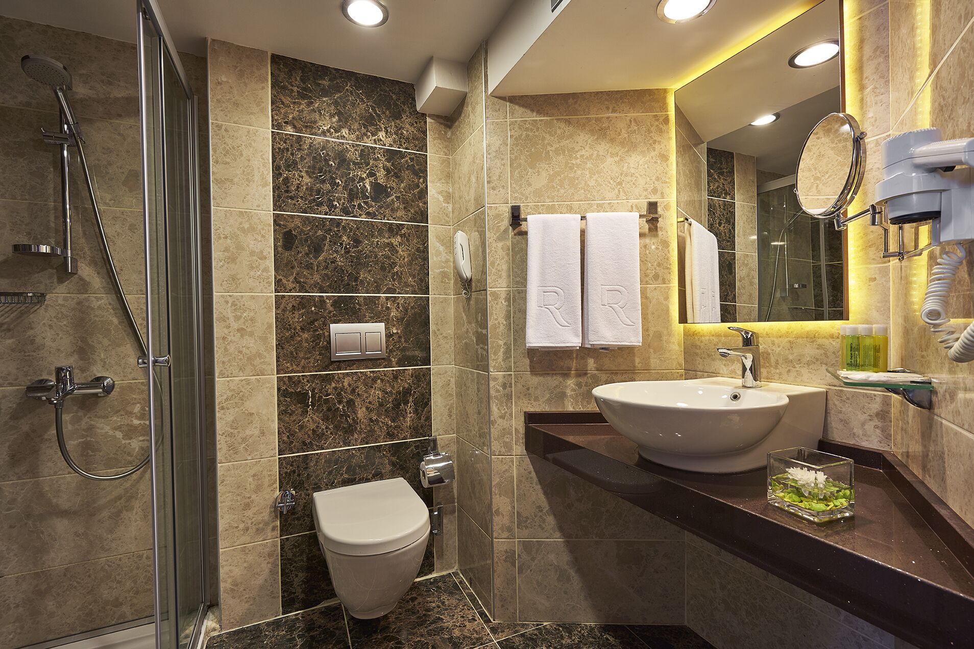 Un baño moderno con ducha de vidrio, inodoro, lavabo con espejo y barra para toallas.