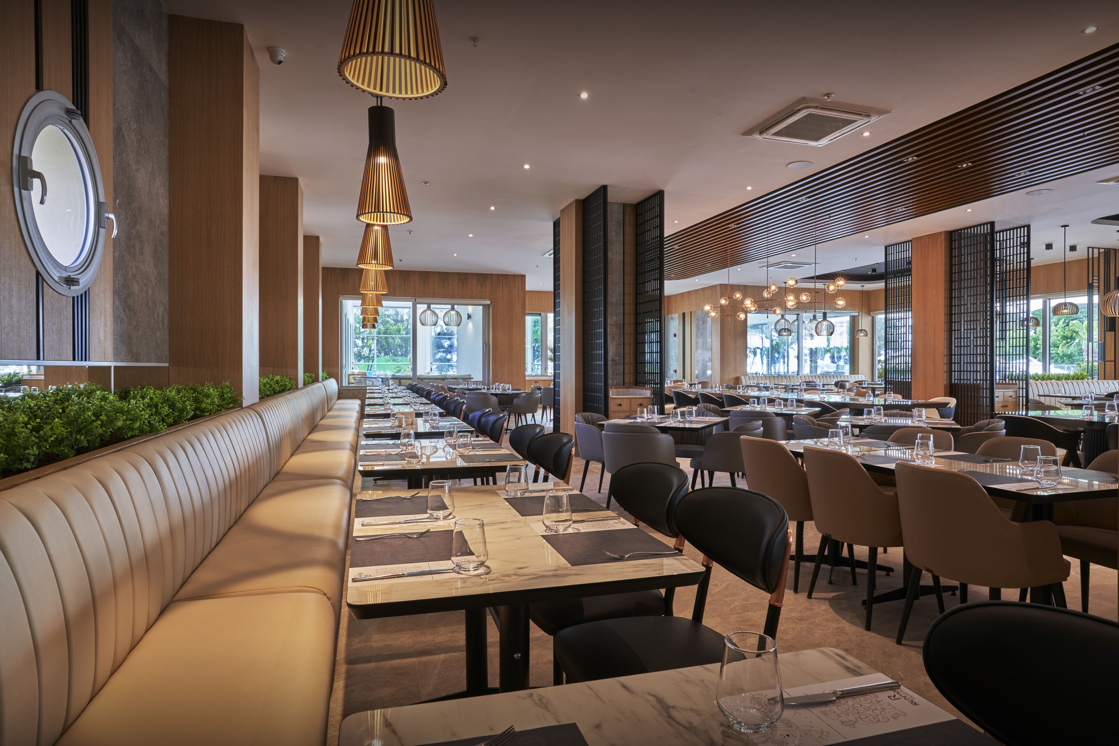 Un restaurante moderno con mesas largas comunitarias, asientos acolchados e iluminación colgante.