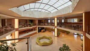 A multi-level atrium with a central seating area, glass railings, and a high ceiling with a skylight. - Richmond Ephesus Resort - All Inclusive (Selçuk)
