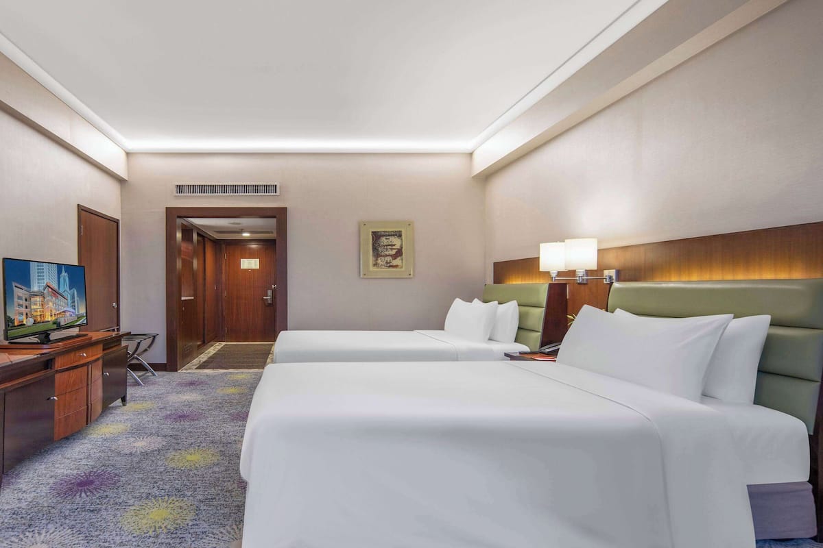 Een hotelkamer met twee bedden, een bureau met een televisie, een ingelijst schilderij aan de muur, en een vloerkleed met een bloemenpatroon.