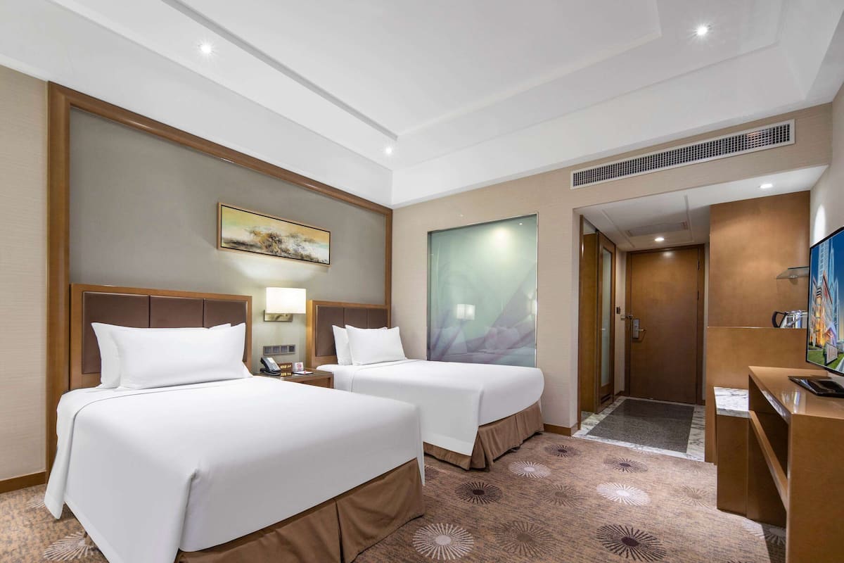 Een hotelkamer met twee bedden, een bureau, een televisie en een deur die naar een andere kamer leidt.