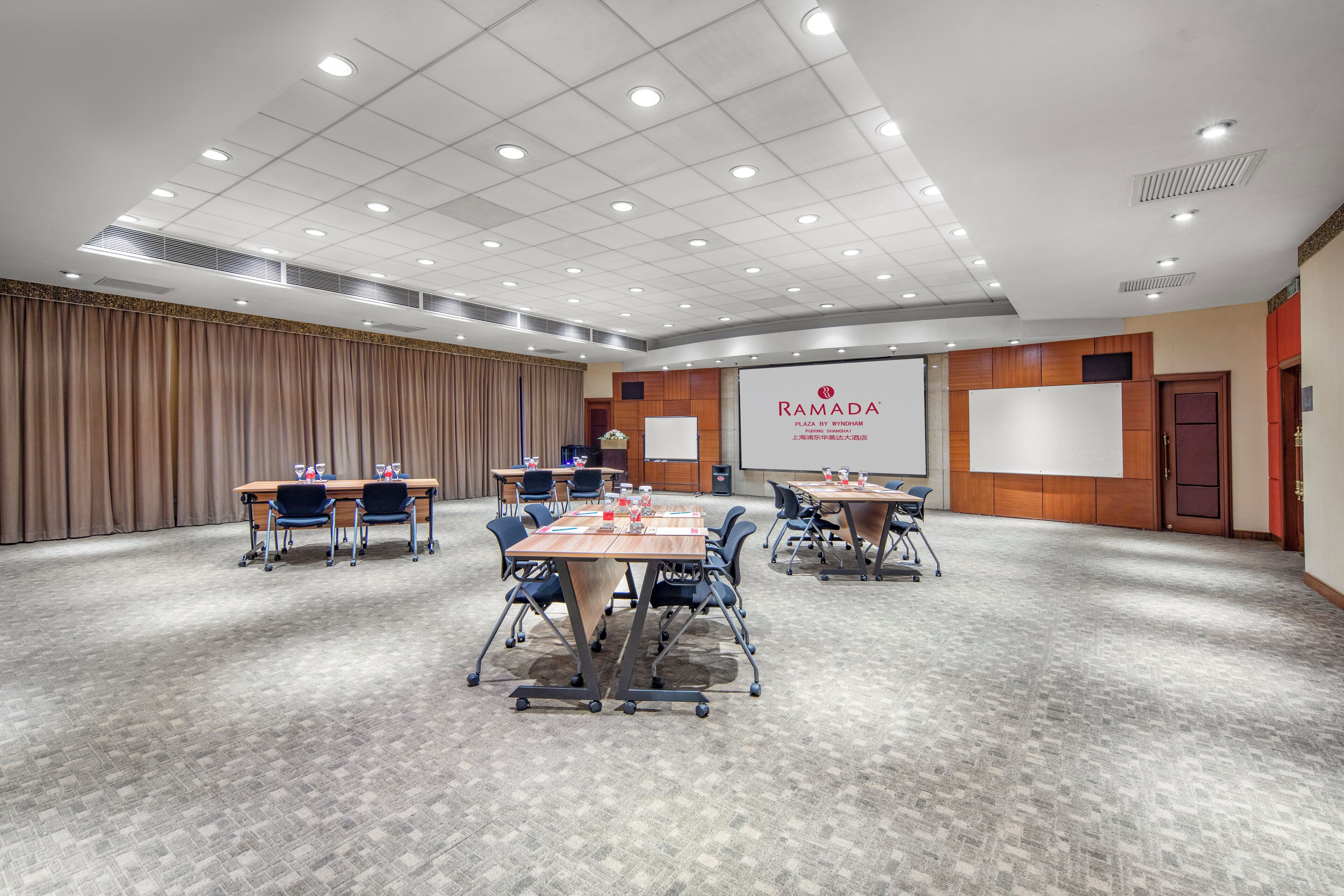 Una sala de conferencias con varias mesas y sillas, una pantalla grande y una zona para presentaciones.