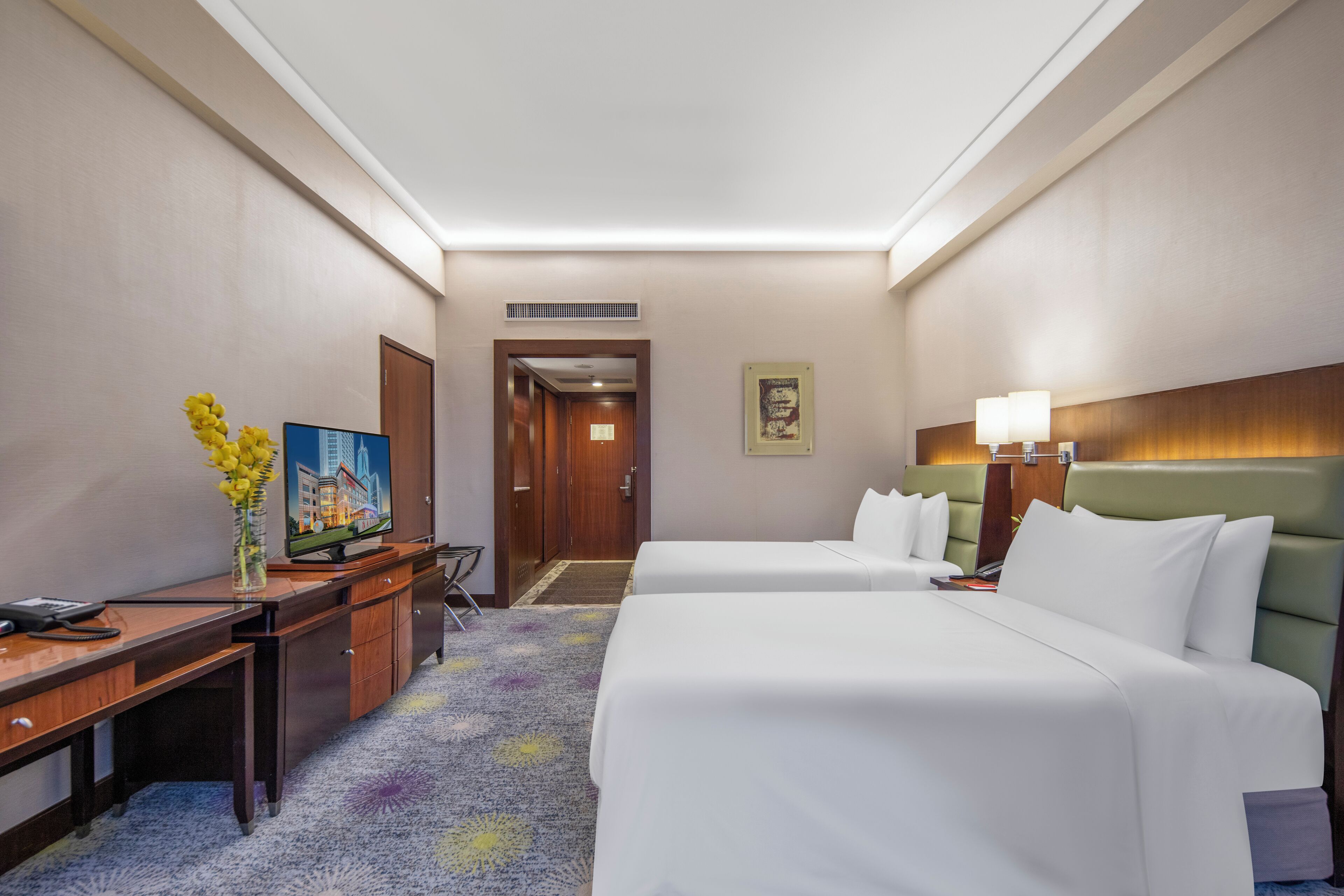 A hotel room with two beds, a desk, a chair, a television, and a door leading to a hallway.