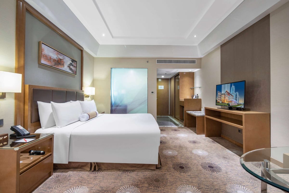 Een hotelkamer met een bed, nachtkastjes, een televisie en een badkamer zichtbaar door een geopende deur.
