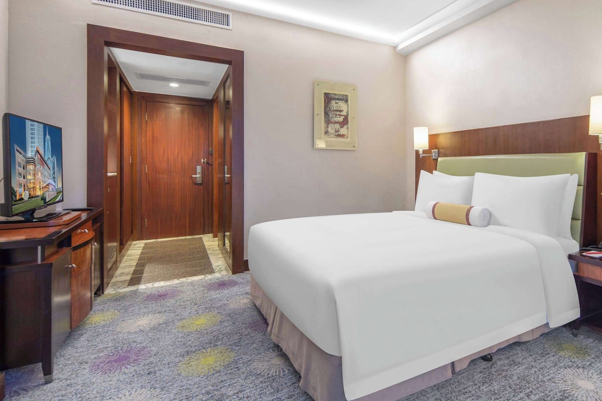 Een hotelkamer met een groot bed, een bureau met een televisie, een deur en een ingelijst schilderij aan de muur.