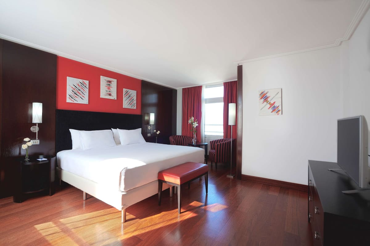 A hotel room with a large bed, a bench, a desk, and a TV.