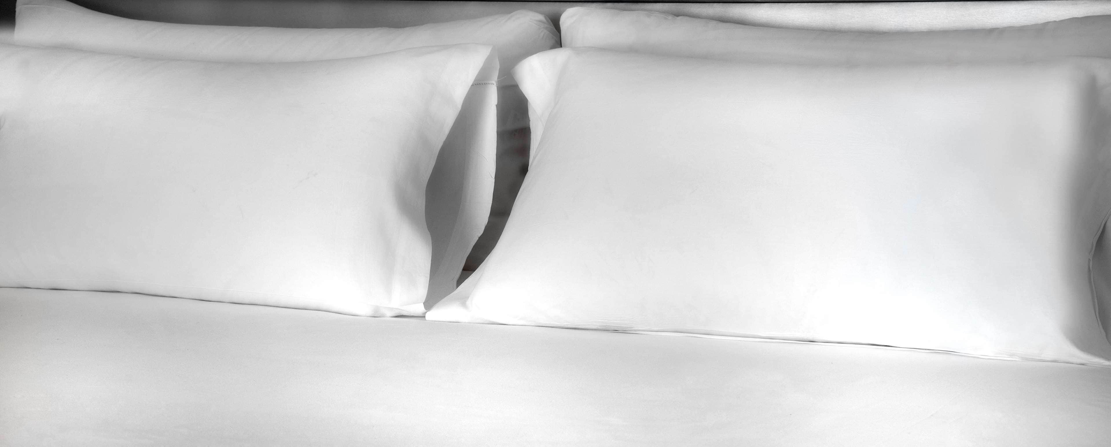Una cama bien tendida con sábanas y almohadas blancas.