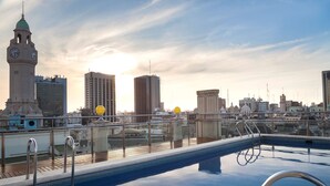 Una piscina en la azotea con el horizonte de la ciudad al fondo, incluyendo una torre del reloj y edificios modernos.