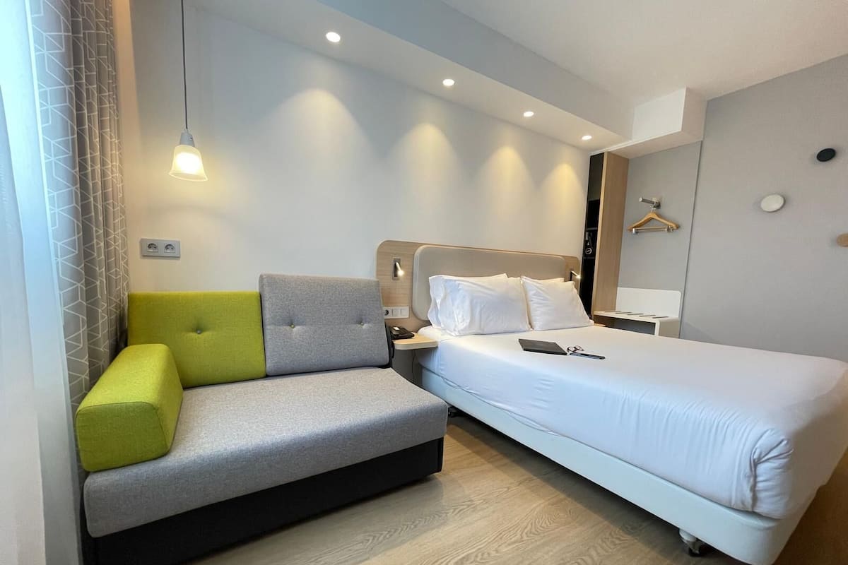 Una habitación de hotel moderna con sofá, cama y mesita de noche.