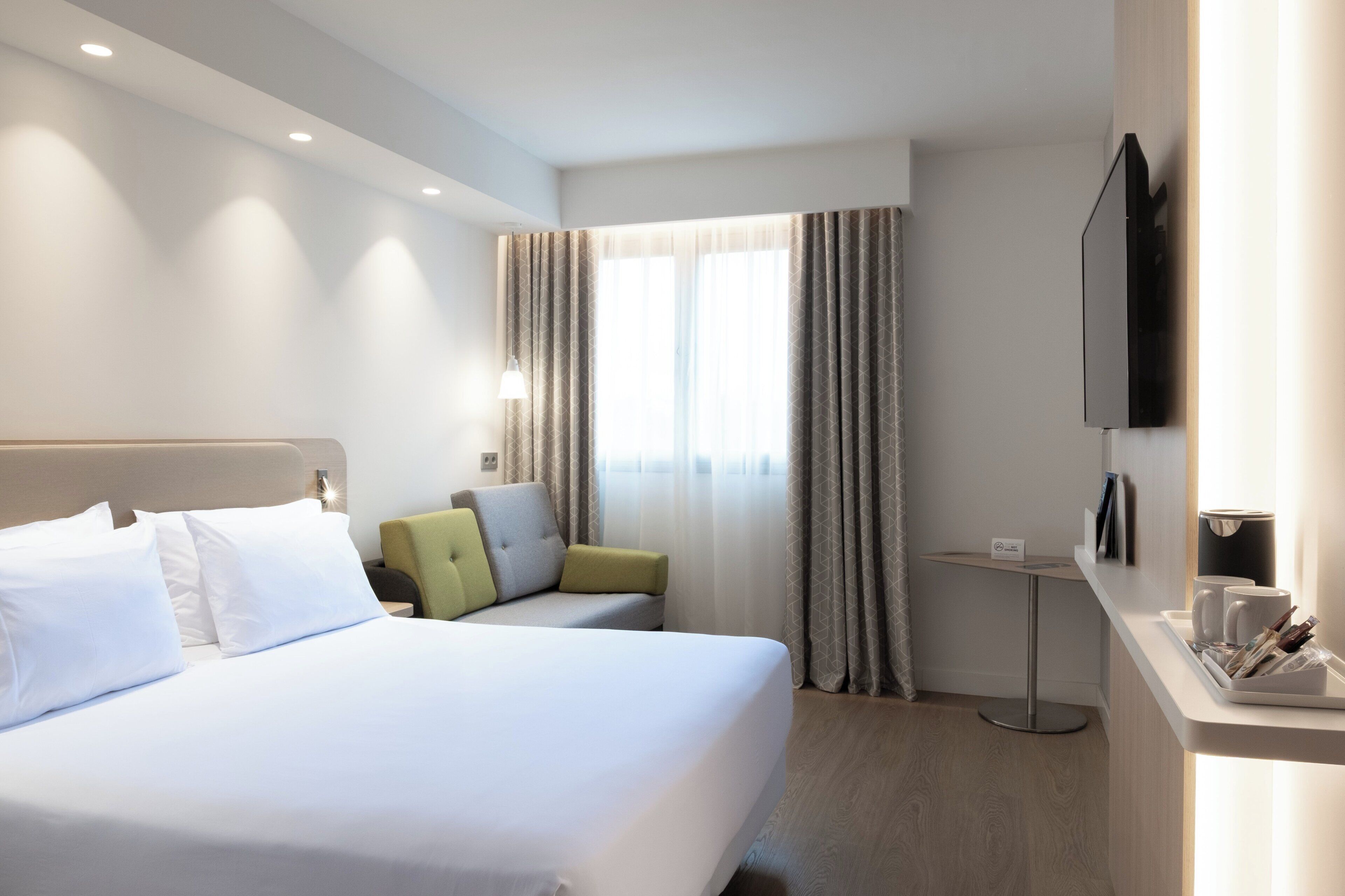 Une chambre d’hôtel avec un grand lit, un petit canapé, un bureau avec un téléviseur à écran plat et une fenêtre avec des rideaux.