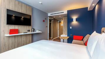 Una camera d'hotel con un letto, una TV a parete, un tavolino e una sedia rossa.