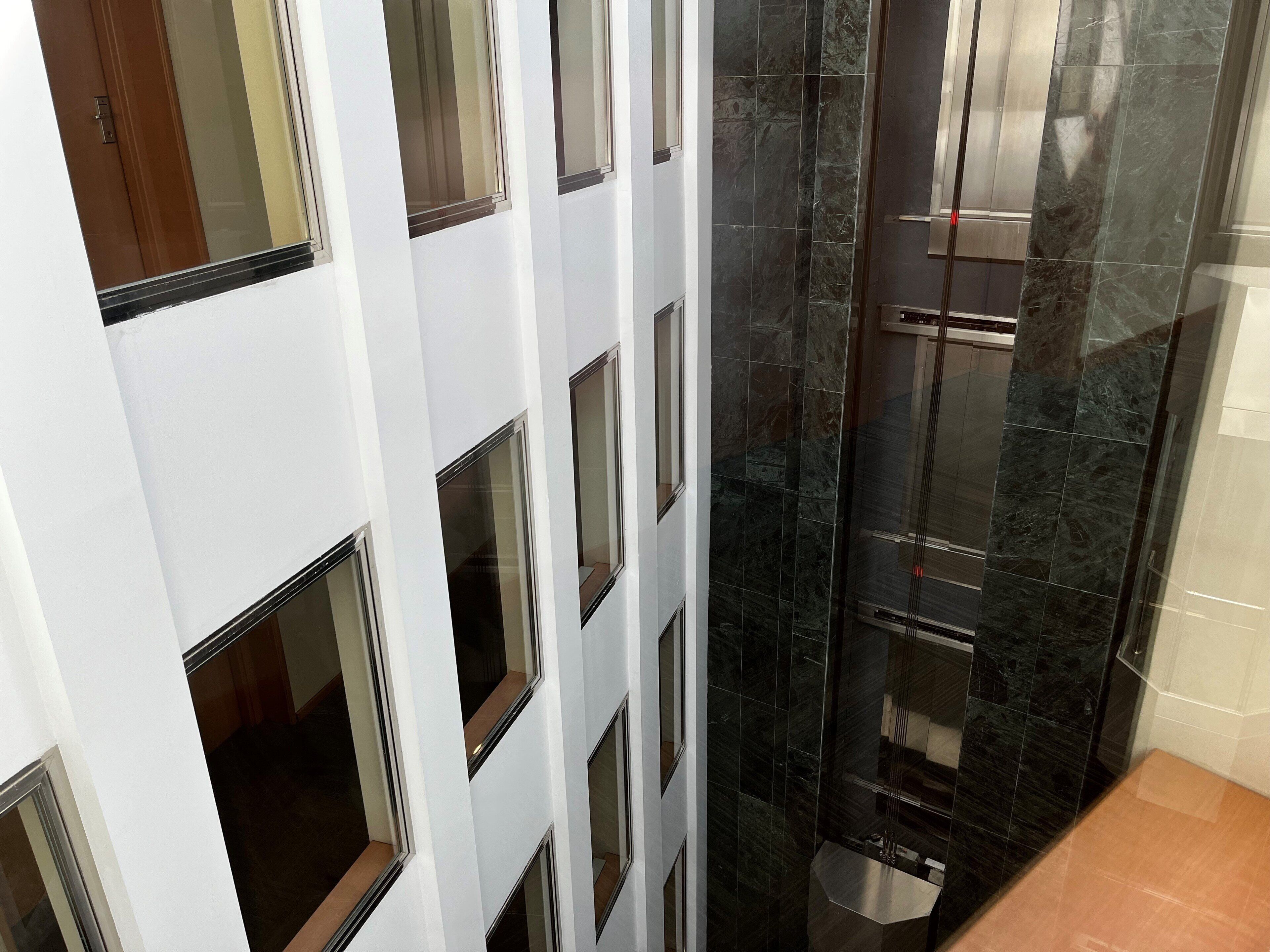 A modern bathroom with dark marble tiles, a glass shower enclosure, and a white wall with multiple windows.