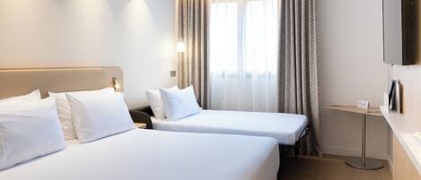 A hotel room with two beds, a TV mounted on the wall, a bedside table, and a window with curtains.