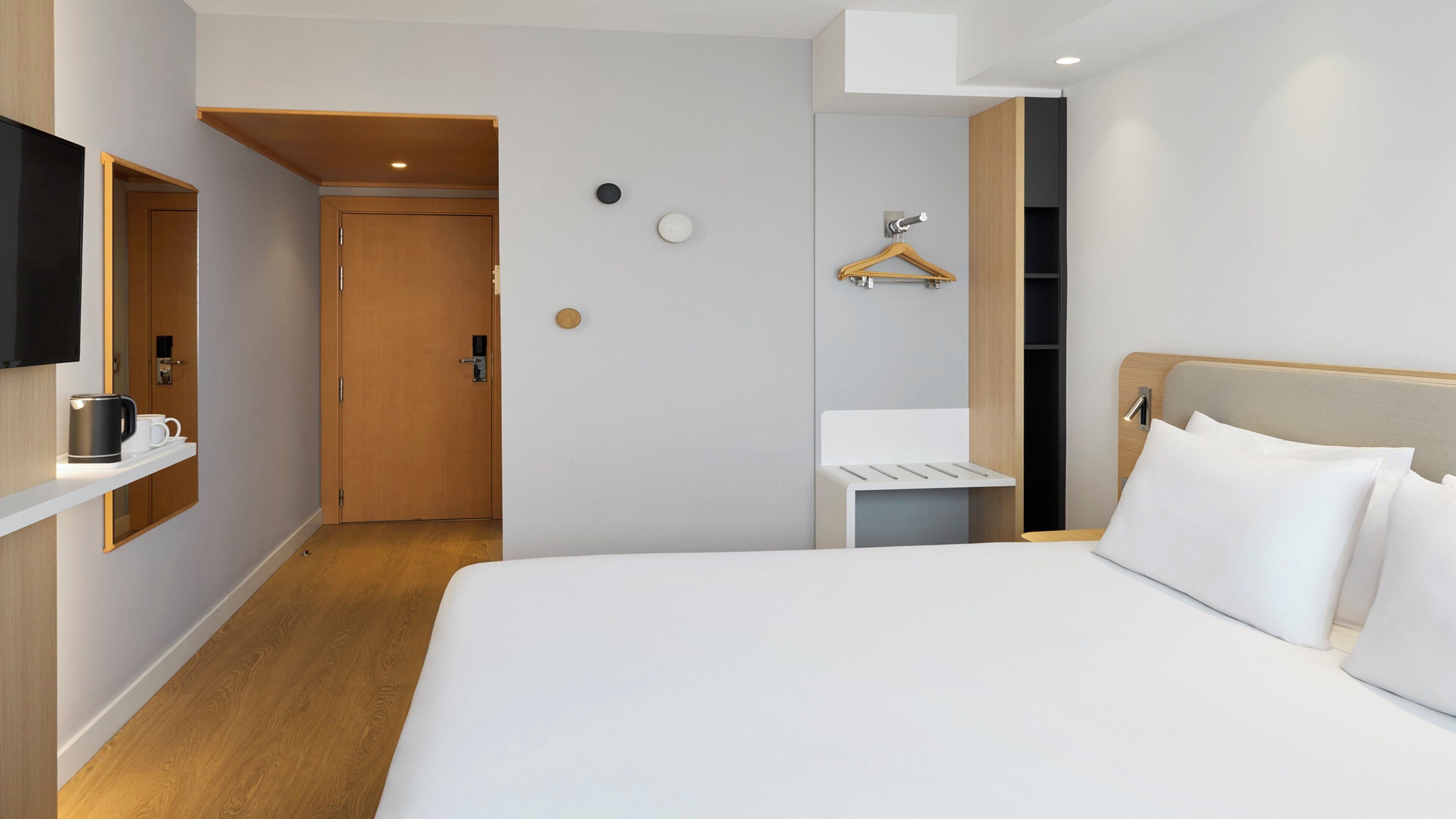 Een hotelkamer met een bed, een televisie, een koffiezetapparaat, een spiegel en een houten deur.