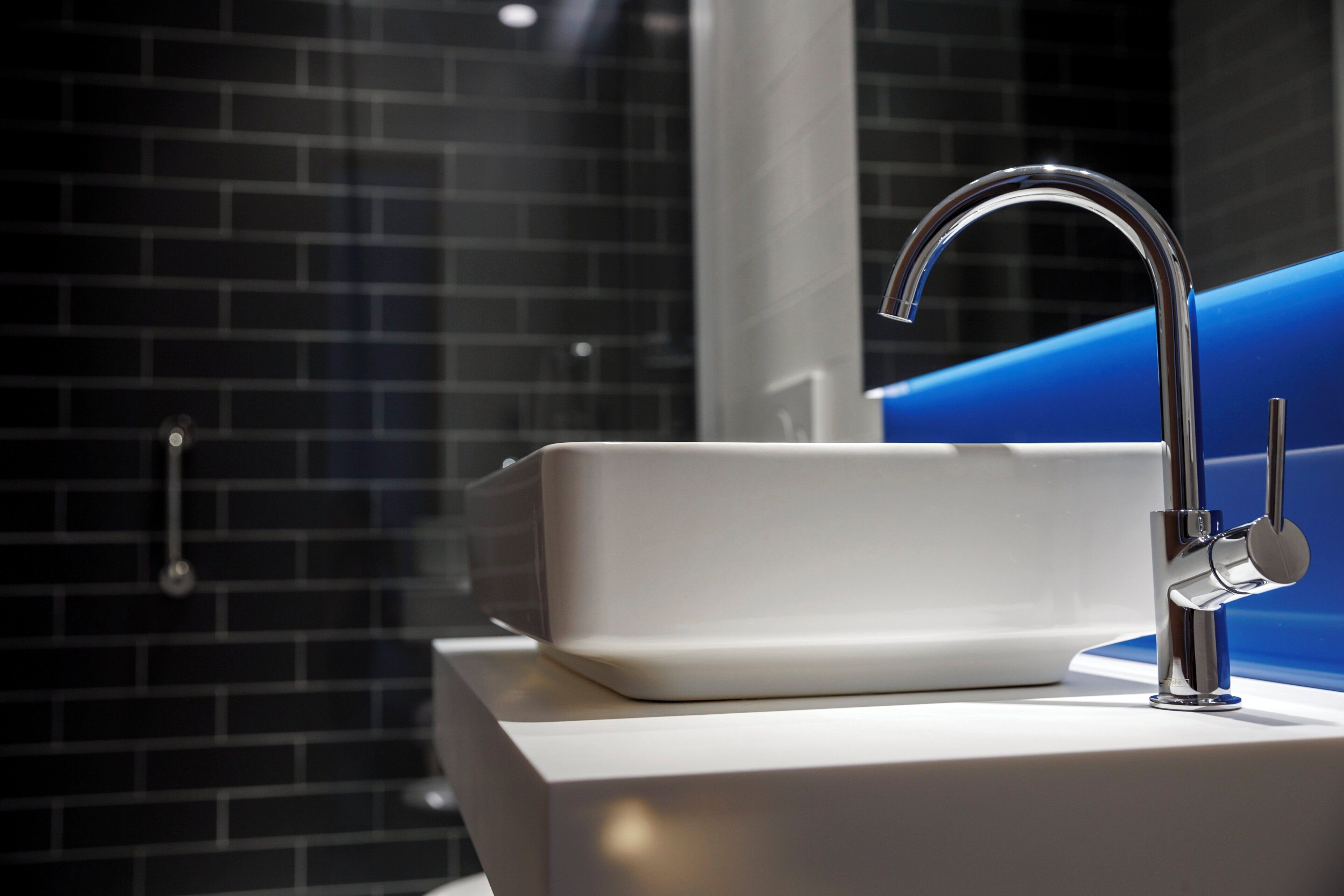 A modern bathroom with a white sink and chrome faucet, set against a dark brick wall.