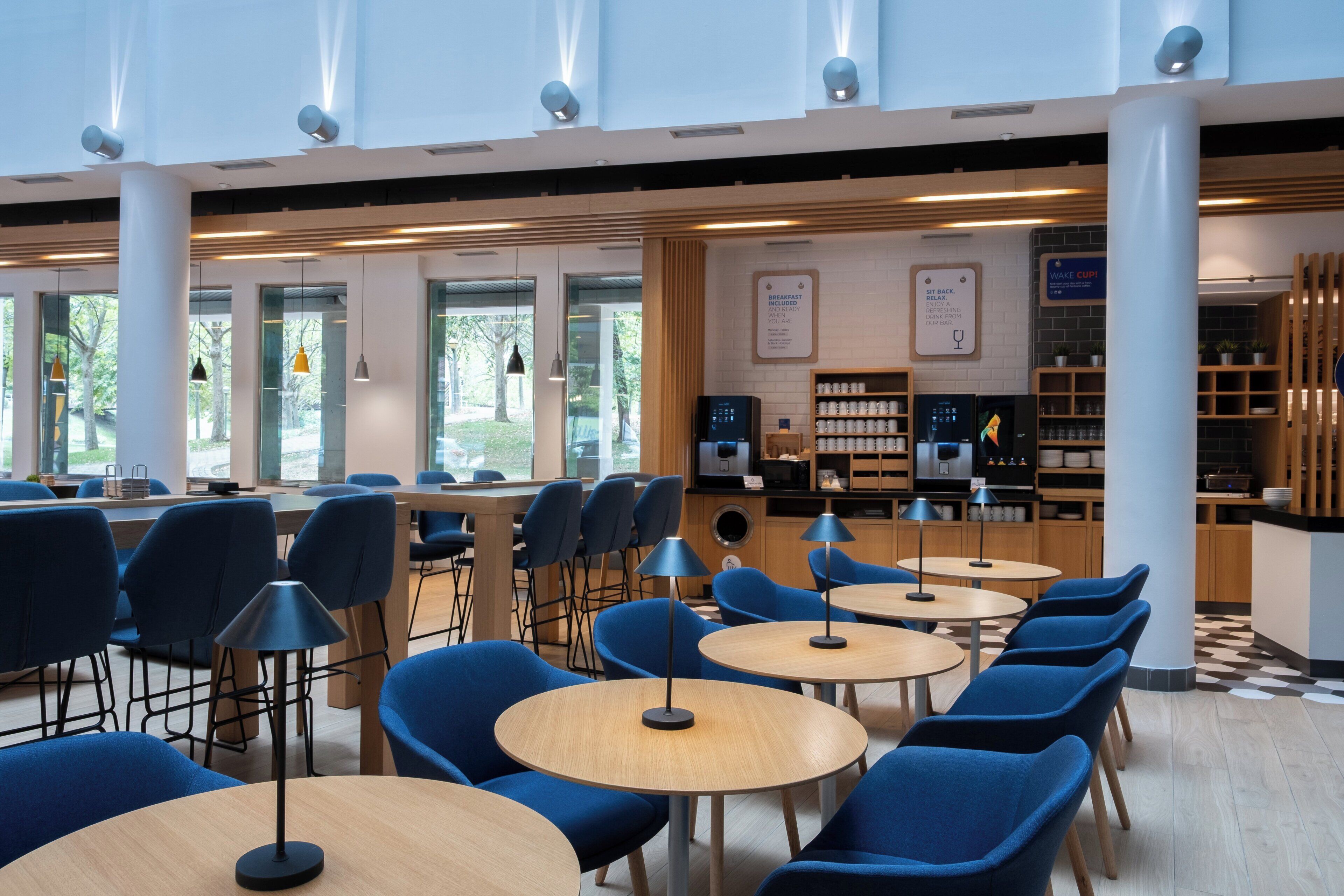 A modern cafe with round tables, blue chairs, and a coffee machine.