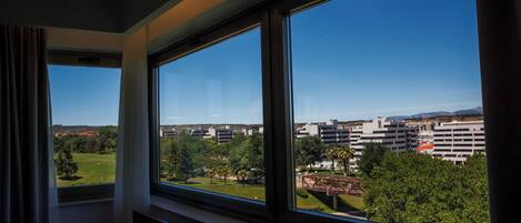 A room with large windows overlooking a cityscape, including buildings and greenery.