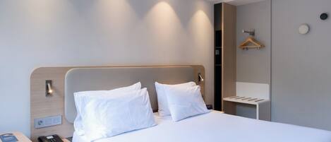A modern hotel room with a large bed, a bedside table with a phone, and a small desk with a chair.