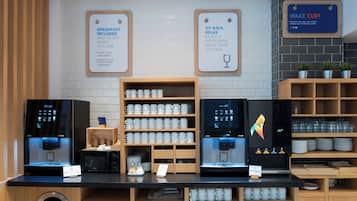 A coffee station with multiple coffee machines, a sign indicating breakfast is included, and a sign encouraging guests to sit back and relax.