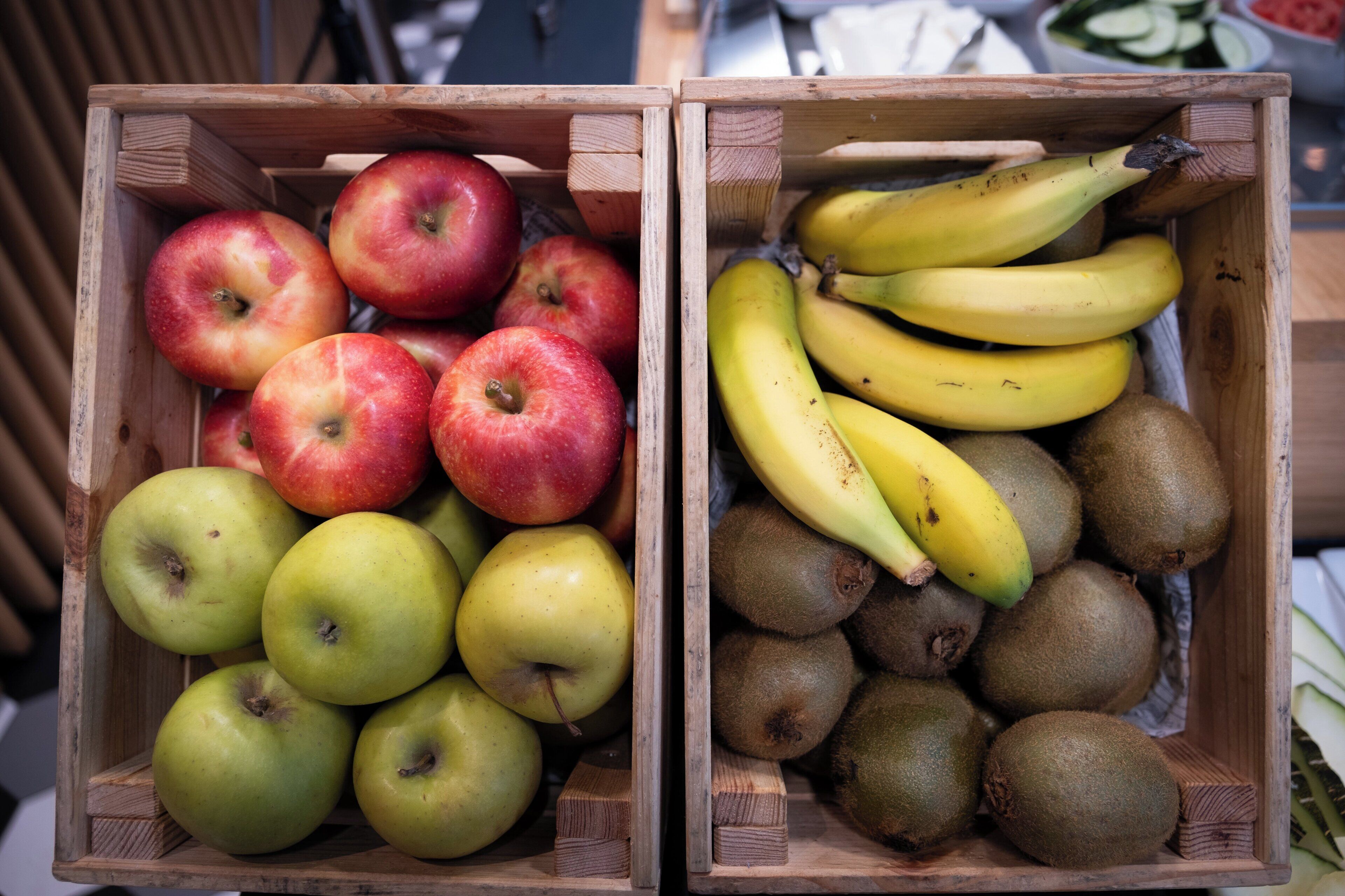 To trækasser, den ene fyldt med æbler og den anden med bananer og kiwier.