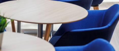 A seating area with round tables and blue chairs, some with potted plants.