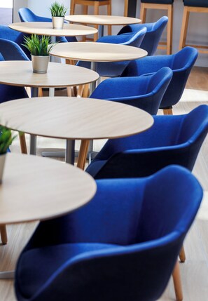 A seating area with round tables and blue chairs, some with potted plants. - Holiday Inn Express Logrono Rioja by IHG (Logroño)