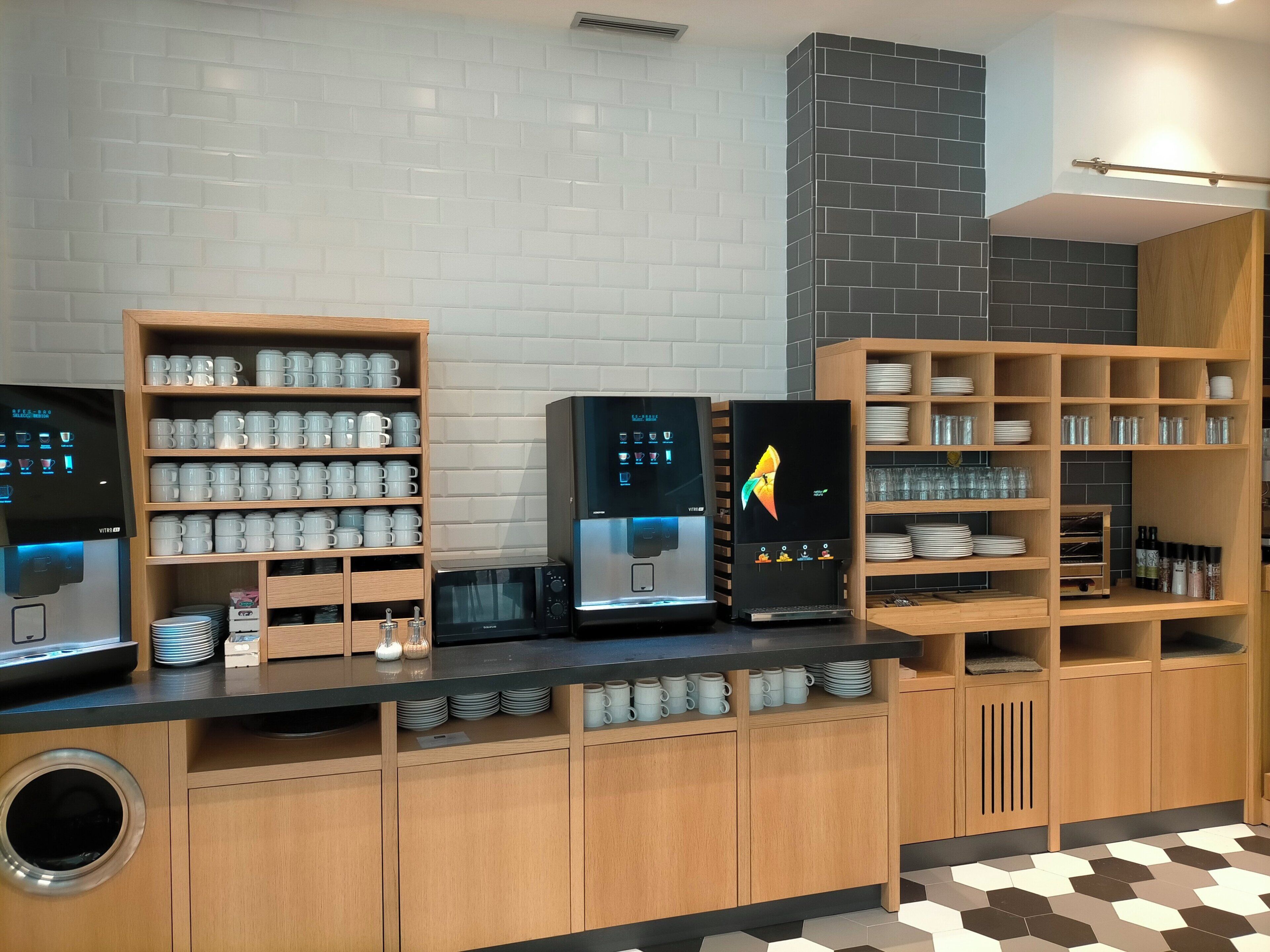 Une cuisine moderne avec des meubles en bois, un four à micro-ondes encastré, une machine à café et des étagères où sont rangées des tasses et de la vaisselle.