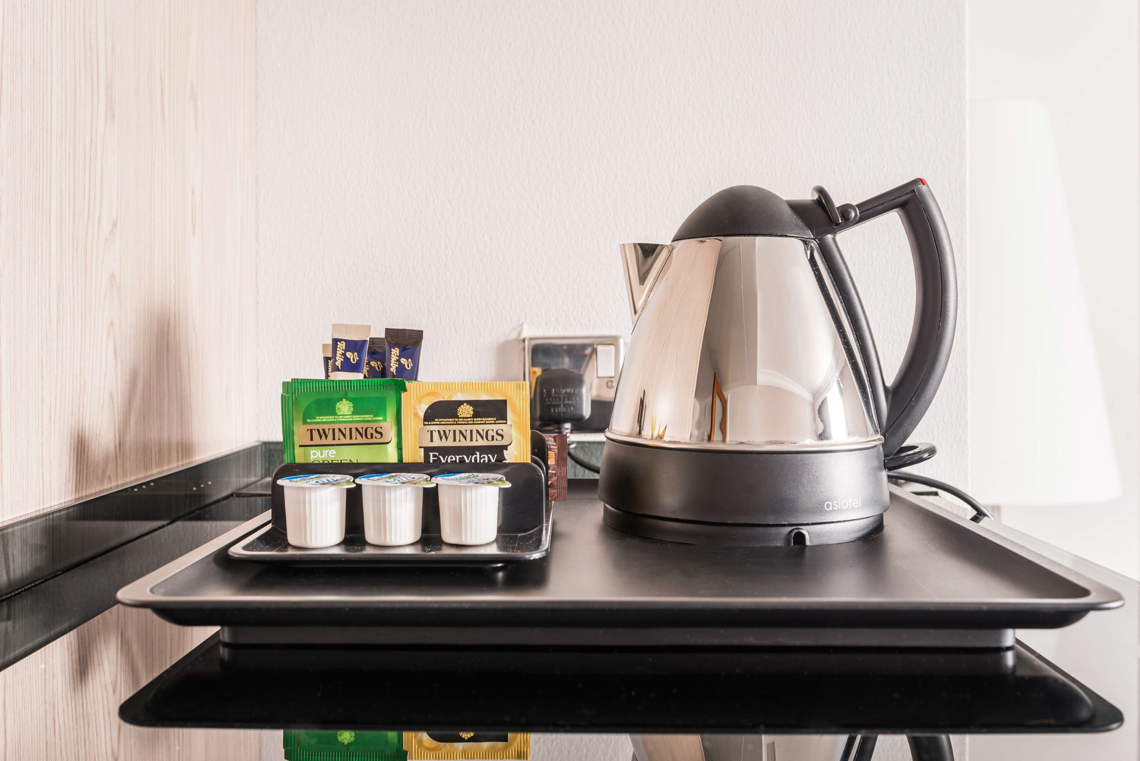 Un comptoir de cuisine avec une machine à café, des boîtes de thé Twinings et un plateau avec des tasses.