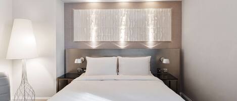 Une chambre d’hôtel moderne avec un grand lit, deux tables de chevet, un luminaire fixé au mur et un panneau décoratif au-dessus du lit.