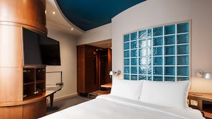 A hotel room with a large bed, a TV mounted on a wooden cabinet, a window with blue-tinted glass, and a door leading to a bathroom. - Radisson Blu Hotel, Leeds City Centre (Leeds)
