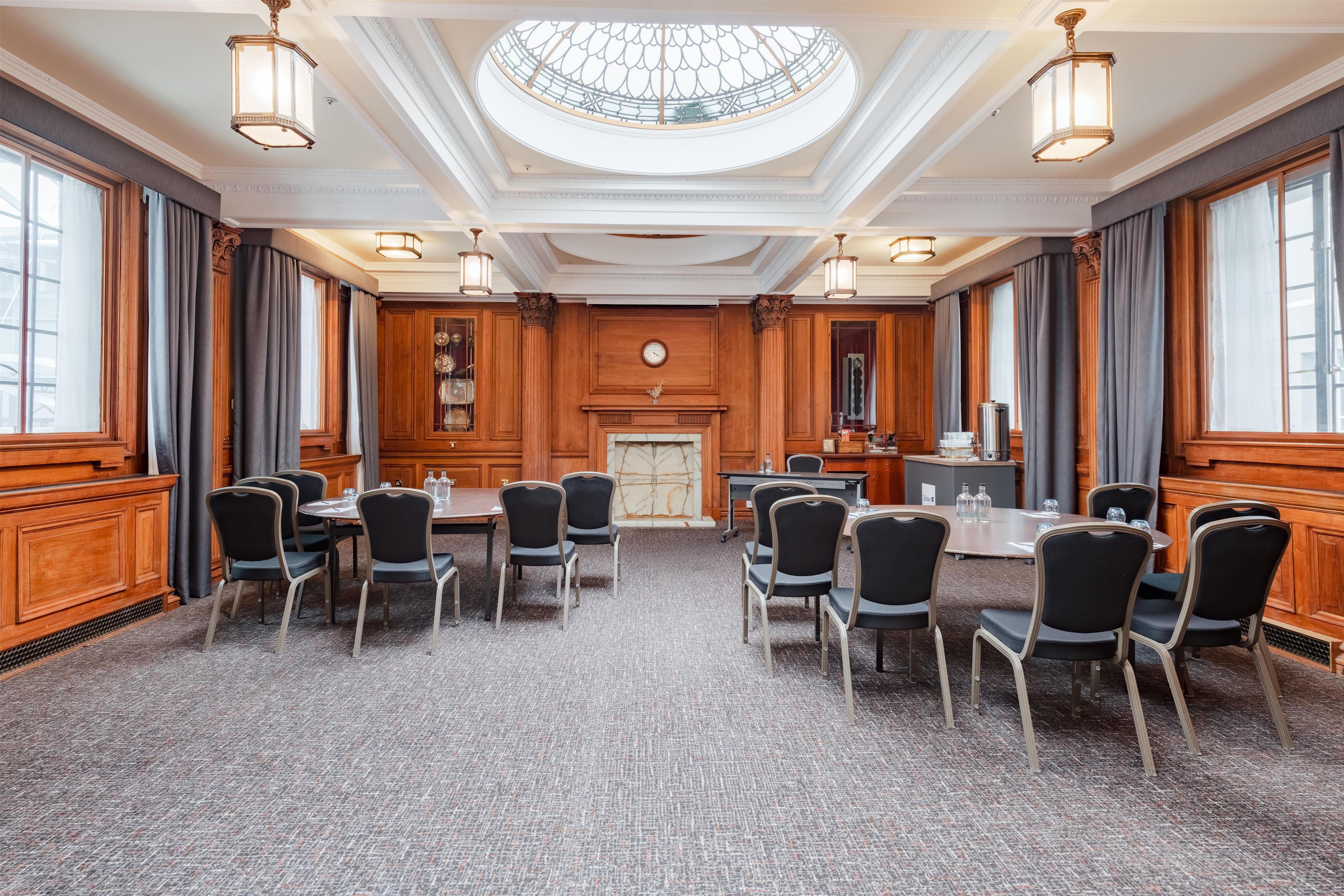 A conference room with a high ceiling, large windows, and a central fireplace.