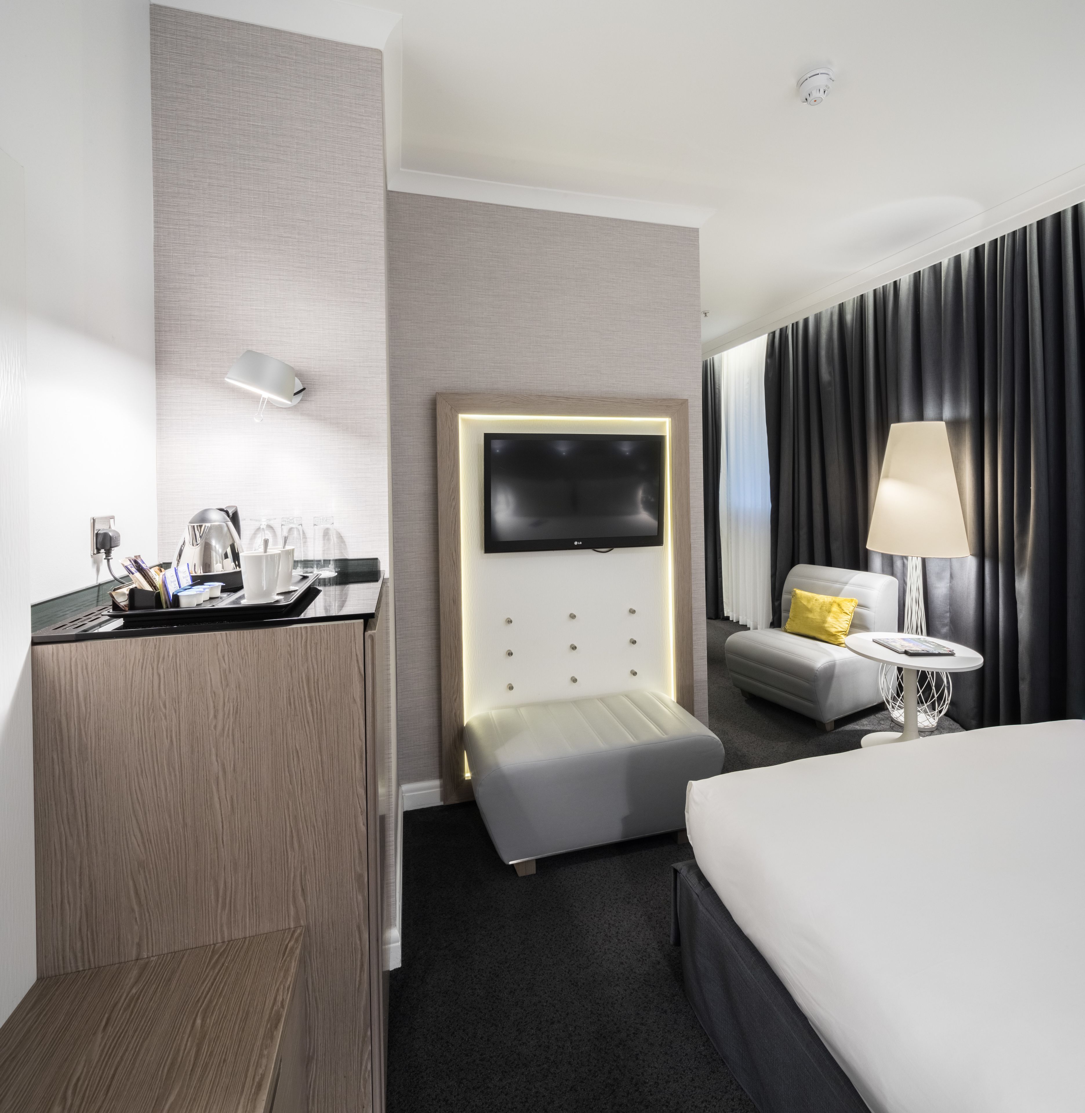Una habitación de hotel moderna con una cama, un escritorio con televisor de pantalla plana, un sofá y una mesita.