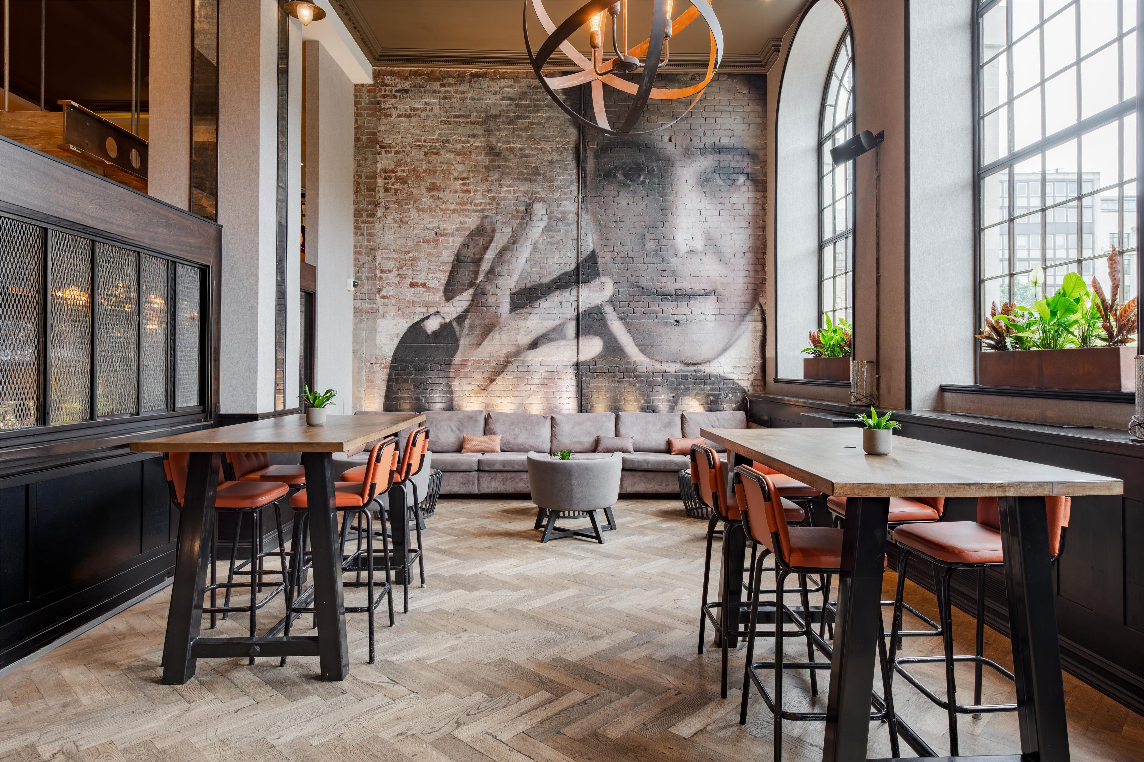 A restaurant interior with a brick wall mural, wooden flooring, and a mix of bar and dining seating.