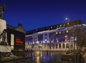 Een historisch gebouw met een Radisson BLU hotelschilt, een standbeeld en een goed verlicht plein.