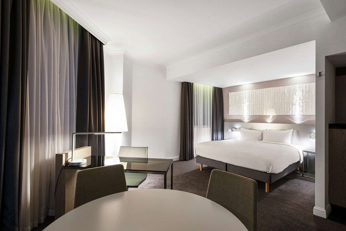 Ein Hotelzimmer mit Bett, Nachttischen, Schreibtisch, Stuhl und rundem Tisch.