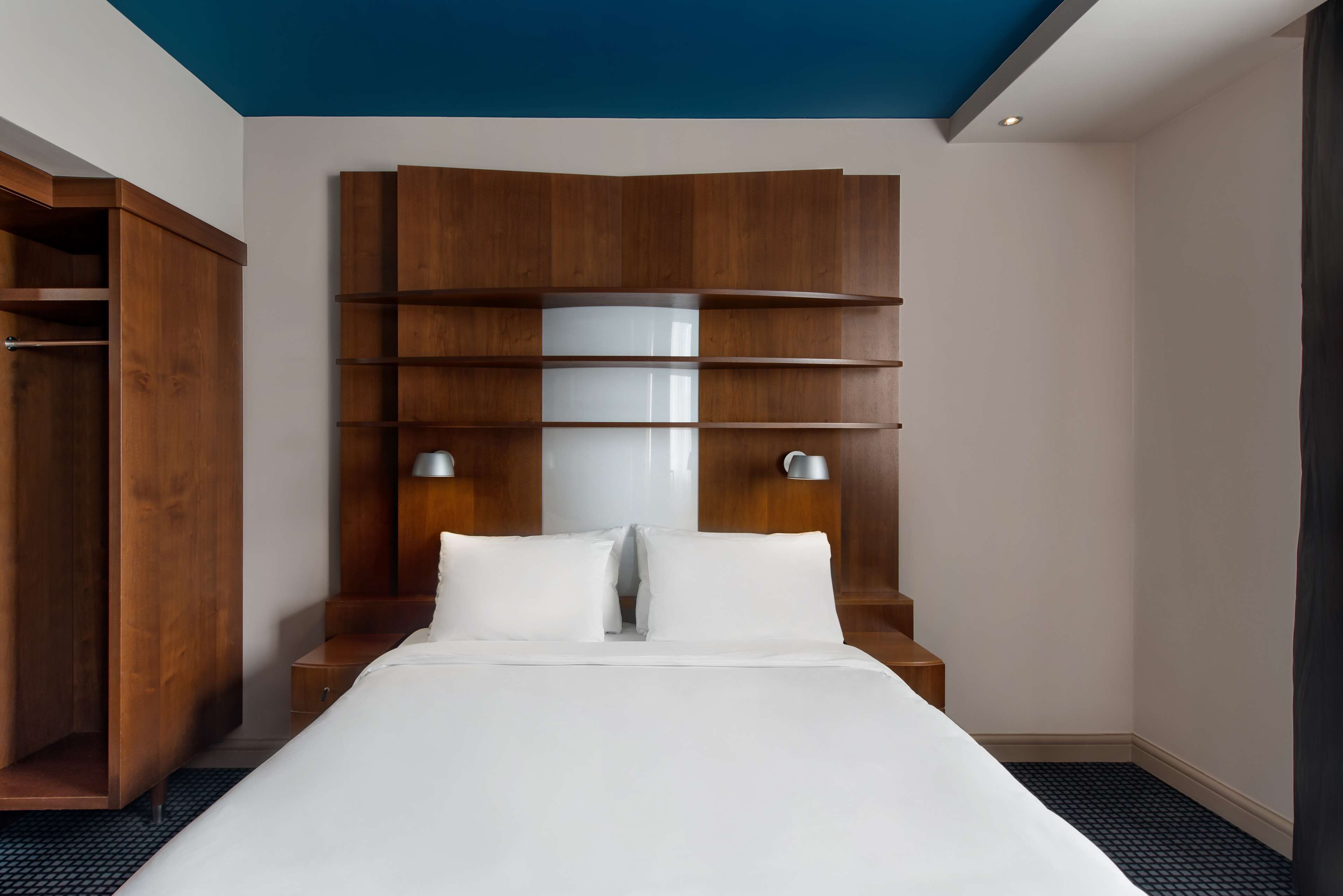 A modern hotel room with a large bed, wooden headboard, and built-in shelves.