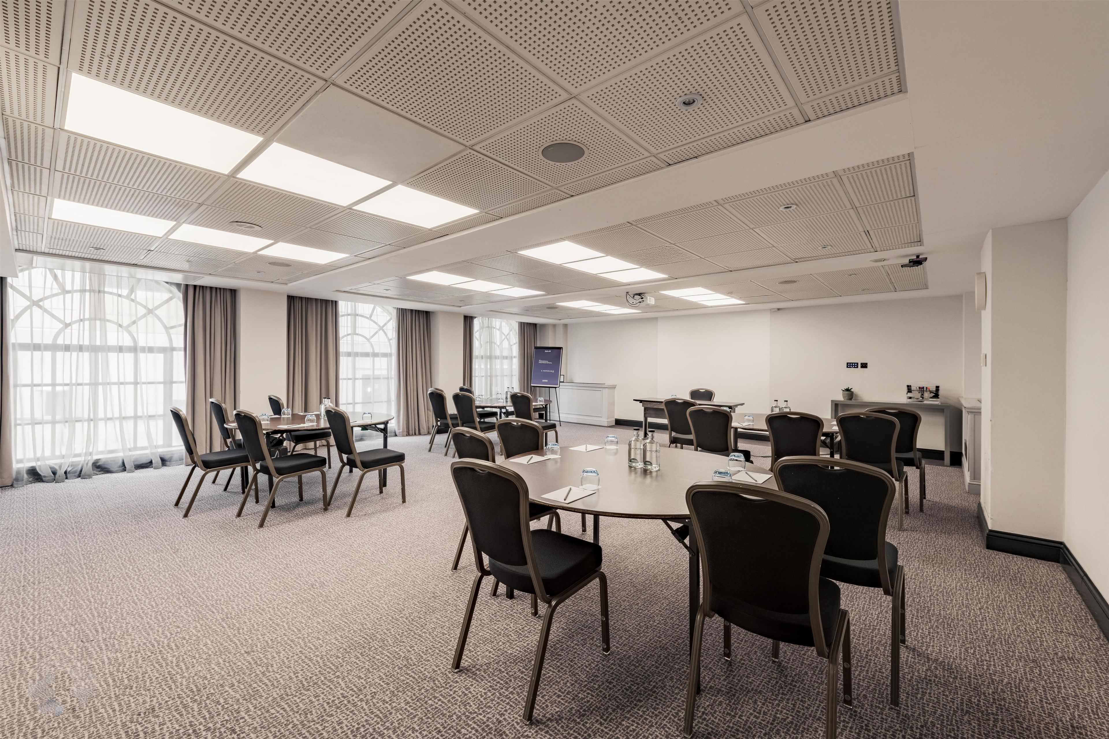 Ein Konferenzraum mit hoher Decke, großen Fenstern und einer Projektionsleinwand.