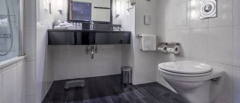 A modern bathroom with a black vanity, a large mirror, a toilet, and a shower area.