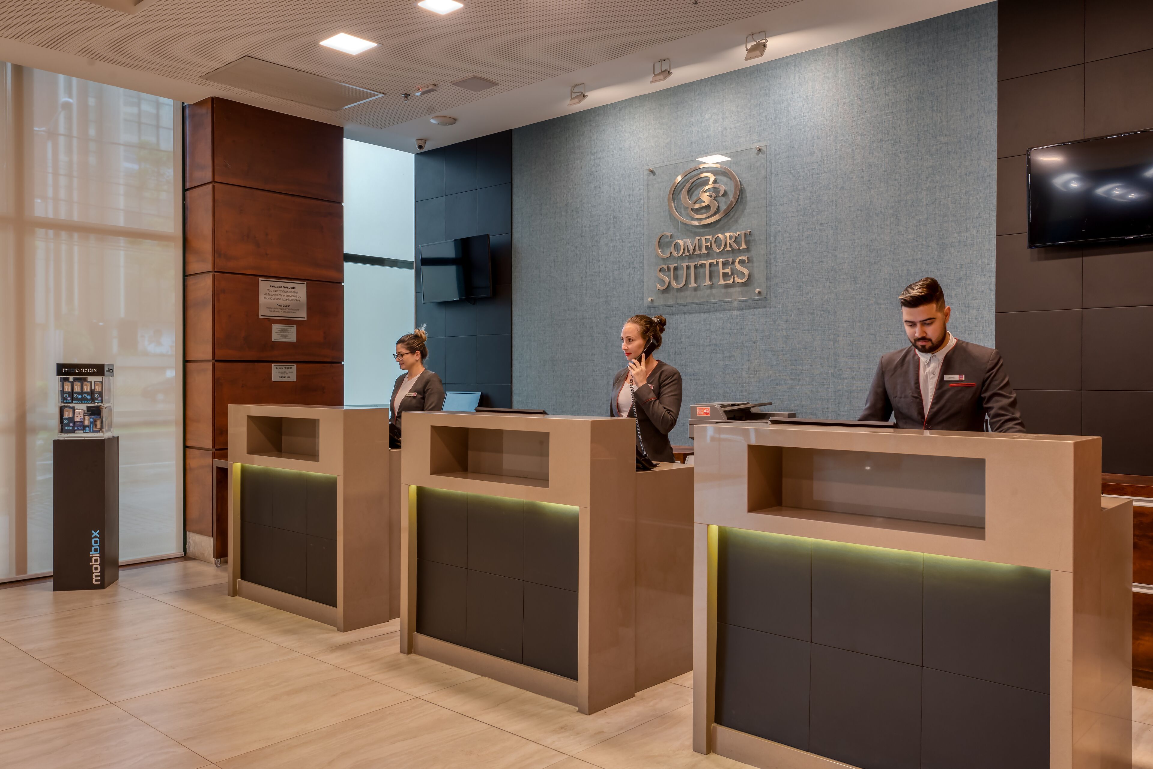 A reception area with three receptionists at desks, a 'Comfort Suites' sign, and a 'mabox' display.