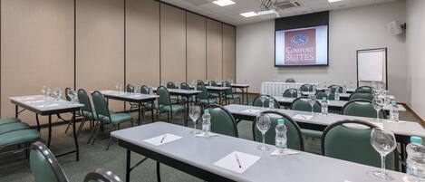 Un salón de conferencias con mesas, sillas, botellas de agua y una pantalla de presentación que muestra