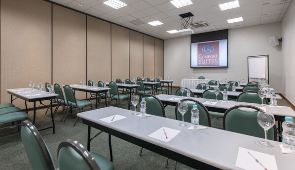 A conference room with tables, chairs, water bottles, and a presentation screen displaying "Comfort Suites". - Comfort Suites Vitoria (Vitoria)