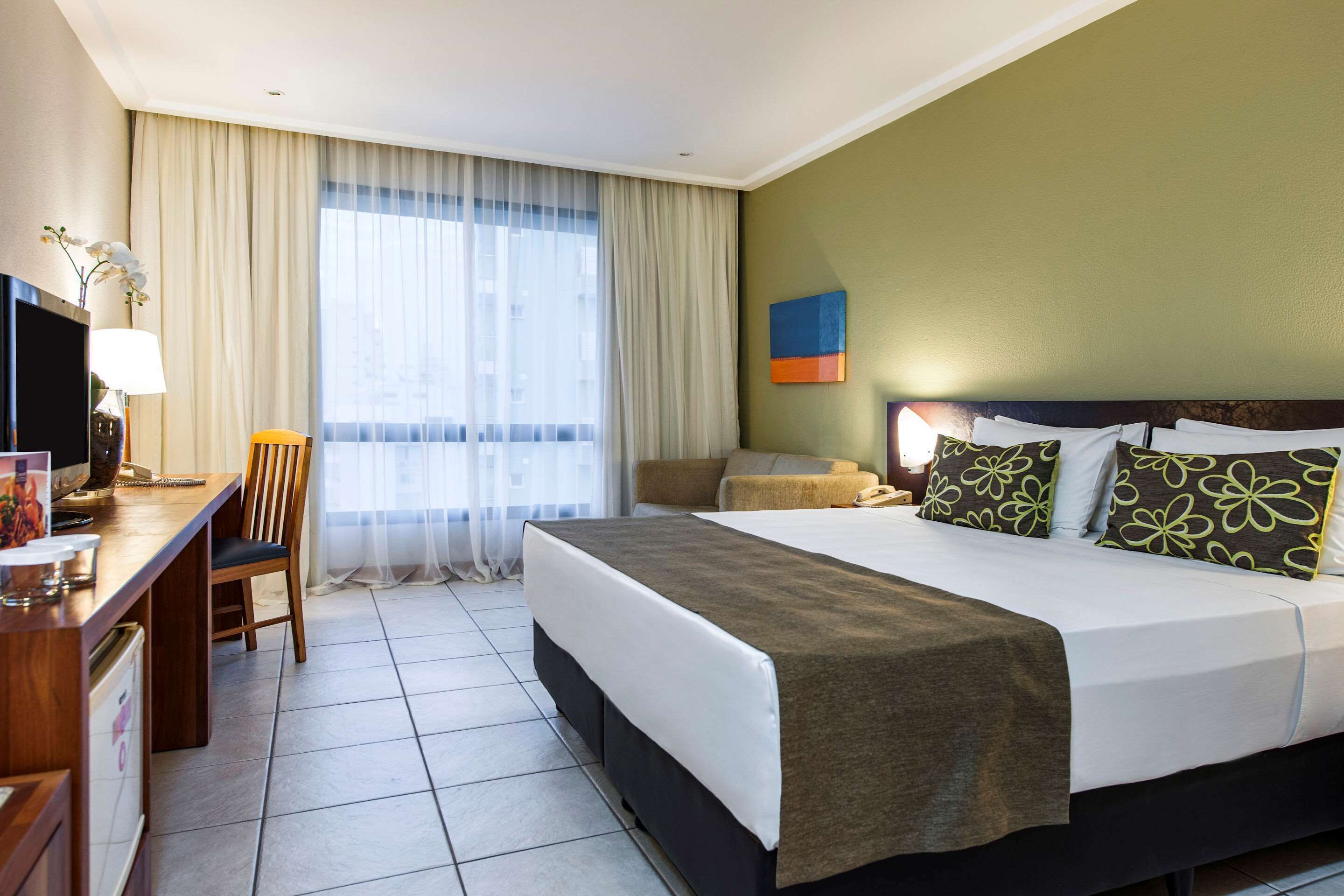 A hotel room with a bed, a desk, a chair, a television, and a window with curtains.